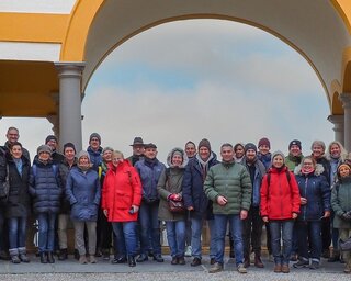Die Gruppe von Menschen steht unter einem bunten Bogen. Sie lächeln und posieren für das Foto, umgeben von einer freundlichen Atmosphäre.